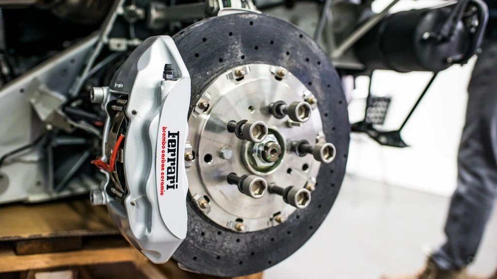Three brake calipers on a steel bench, each tagged to indicate OEM, aftermarket, and remanufactured tiers